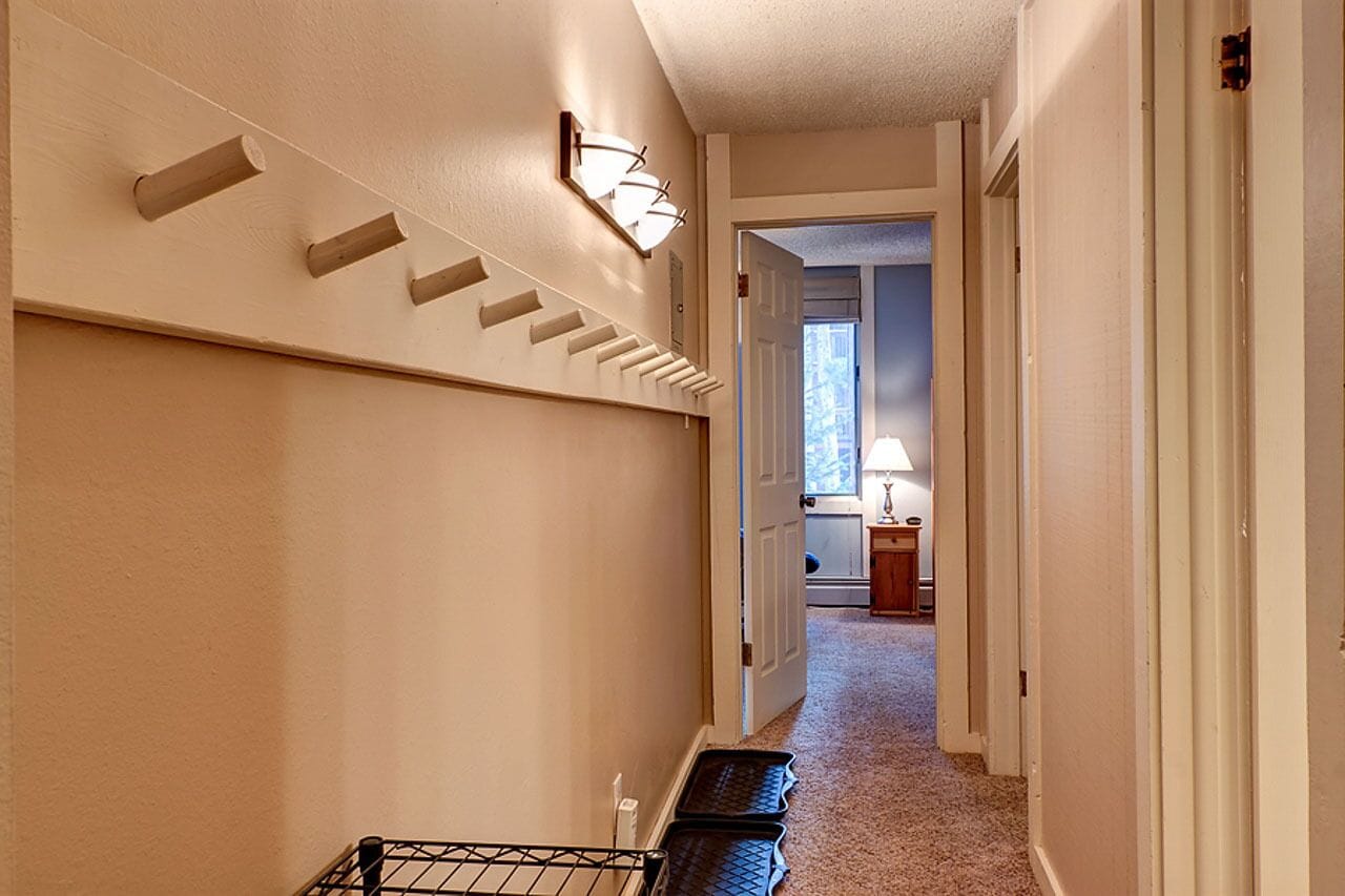 Un couloir avec un escalier, un luminaire fixé au mur et une porte donnant sur une autre pièce.
