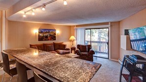 A spacious living area with a large granite island, a sofa, a chair, a TV, and a balcony with a view. - Peak 8 Village Hideaway Condo: On Shuttle Route (Breckenridge)