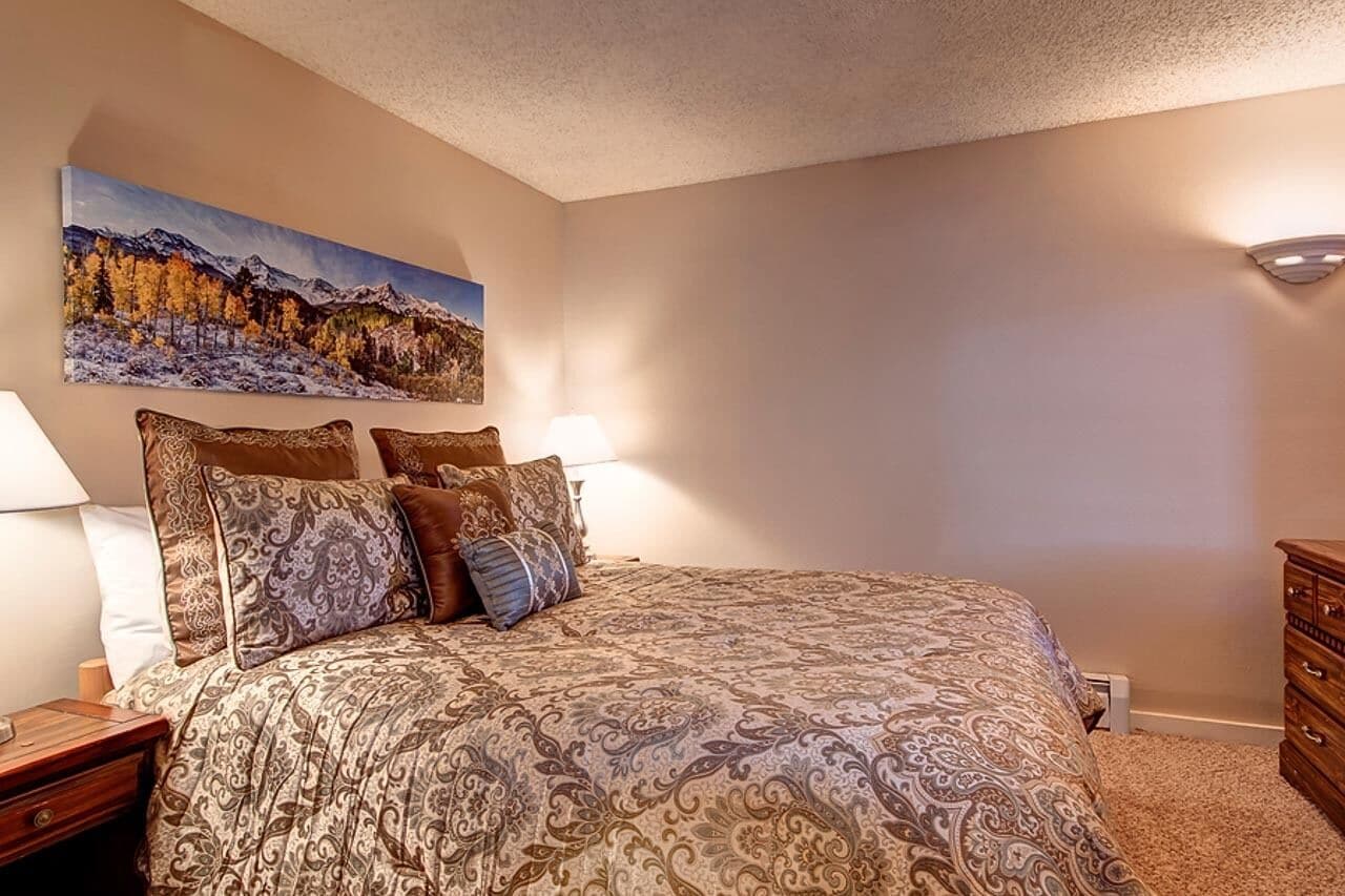 A bedroom with a large bed, a nightstand, a dresser, and a wall-mounted lamp.