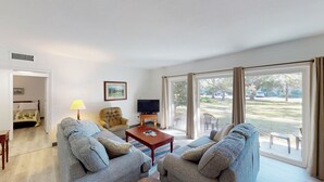 A living room with two sofas, a TV, a lamp, and a window with curtains. - Atlantic Breeze #2 2 bedrooms, 1 bath (Jekyll Island)