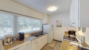 A compact kitchen with white cabinets, a stainless steel sink, a coffee maker, a toaster, and a refrigerator. - Atlantic Breeze #2 2 bedrooms, 1 bath (Jekyll Island)