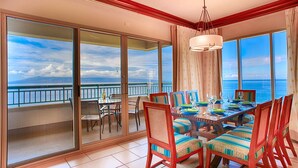 Un comedor con una mesa dispuesta para cuatro, ventanas amplias con vista al mar y un balcón con barandilla.
