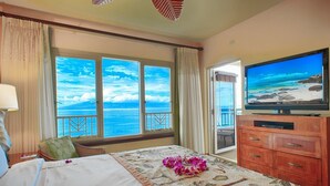 Habitación de hotel con una cama grande, un televisor sobre un mueble de madera y un balcón con vista al océano.