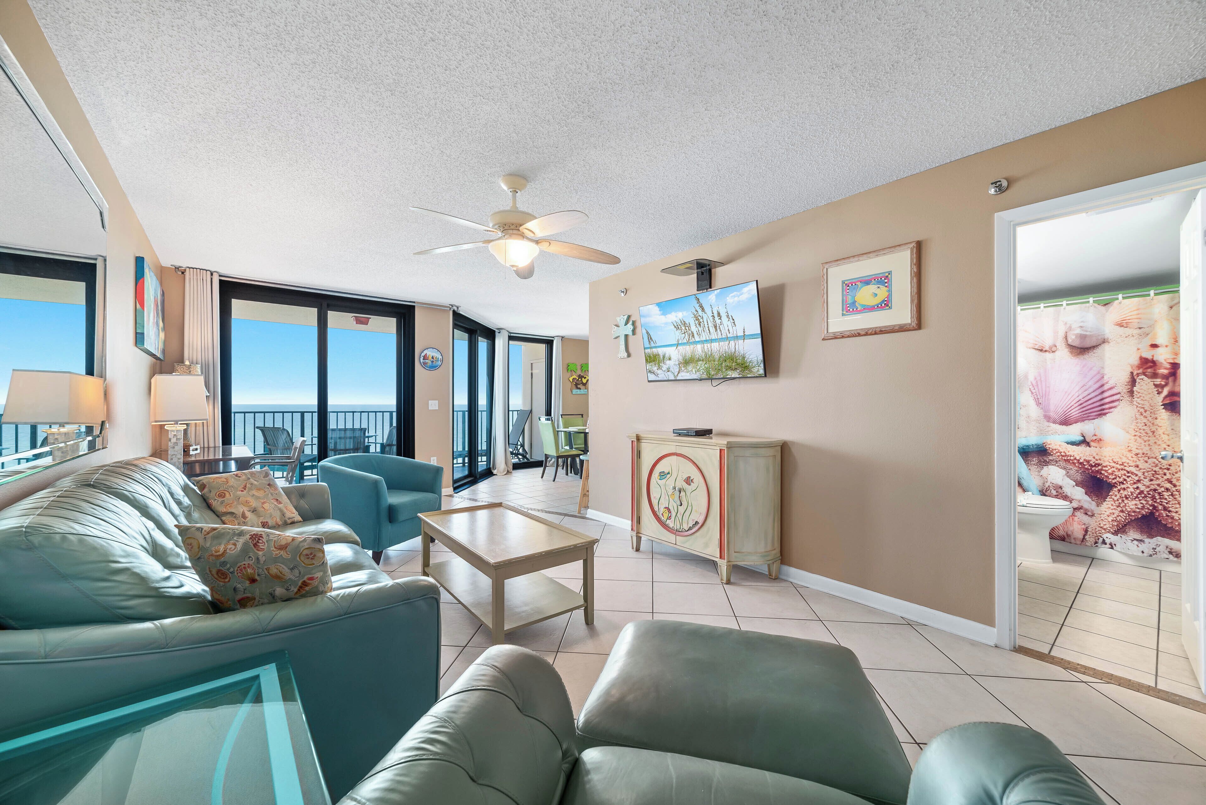 Ein geräumiges Wohnzimmer mit Balkon, Deckenventilator, Flachbildfernseher und dekorativem Schrank.