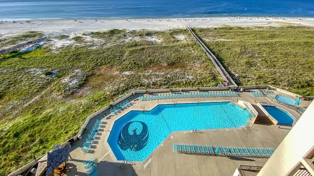 A pool area with a large central pool and smaller side pools, surrounded by lounge chairs and a deck. - Phoenix 7 1011 | Gulf Views | Indoor, Outdoor Pools | My Beach Getaways (Orange Beach)