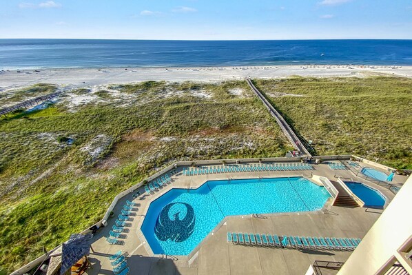 A pool area with a large central pool and smaller side pools, surrounded by lounge chairs and a deck. - Phoenix 7 1011 | Gulf Views | Indoor, Outdoor Pools | My Beach Getaways (Orange Beach)