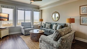 Un salon avec vue sur la plage, un ventilateur de plafond, une table basse ronde et deux fauteuils.