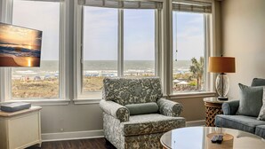 Un salon avec vue sur la plage, un fauteuil à motifs, un canapé, une table basse et un téléviseur fixé au mur.