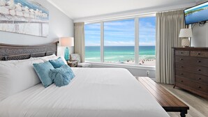 Ein Hotelzimmer mit einem großen Bett, Blick auf den Strand, einem Fernseher und einem Schminktisch.