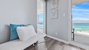 Ein Balkon mit Blick auf den Strand, eine weiße gepolsterte Bank und zwei an der Wand befestigte Kunstwerke.