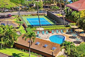 Relax by the pool surrounded by lush greenery and palm trees, with sun loungers and umbrellas providing ample shade.
