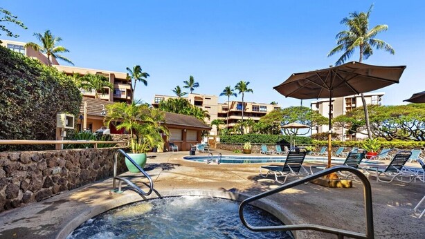 A hot tub surrounded by lounge chairs and umbrellas, with a pool in the background and palm trees. - Kahana Villas E308  Charming Condo (Lahaina)