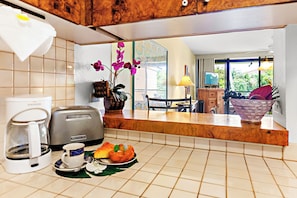 Start your morning with fresh coffee in this charming kitchen, where warm wood tones and tropical touches create a welcoming retreat. Through the window, lush greenery frames your island getaway.