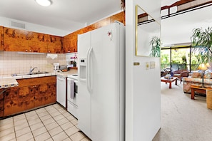 Enjoy cooking in the fully equipped kitchen with a refrigerator, cabinets, and tiled backsplash. Relax in the adjacent living area with a sofa and coffee table.