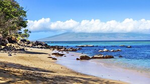 A beach with clear blue water, rocky shoreline, and a mountain in the background. - Kahana Villas E308  Charming Condo (Lahaina)