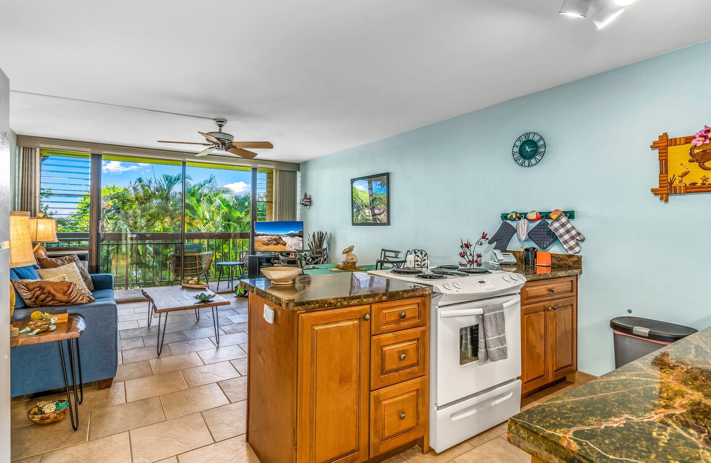 Una cocina con una isla central, armarios de madera, una estufa y un área de comedor con un sofá azul y una mesa.