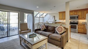 A spacious living area with a glass coffee table, a sofa with decorative pillows, and a sliding glass door leading to an outdoor patio. - 119 Beachwalk - 5 Minute Walk to the Beach - Enjoy a Pet Friendly getaway! (Hilton Head Island)