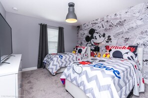 Ein Schlafzimmer mit zwei Betten, einer großen Wandmalerei mit Mickey Mouse und einer Deckenleuchte.