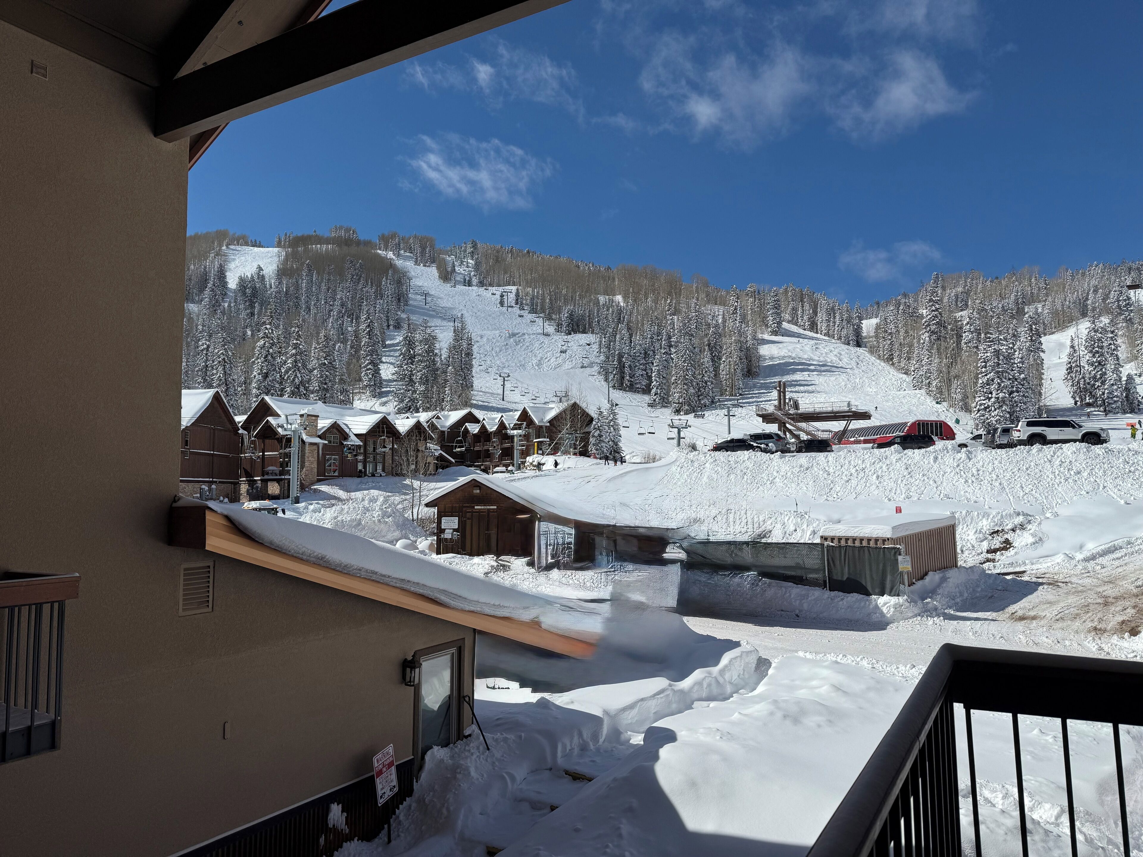 Et snøklædt bjergresort med træhytter, skilifte og en klar blå himmel.