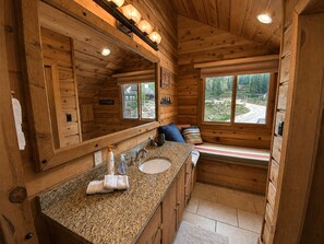 A wooden cabin bathroom with a granite countertop, a sink, a mirror, and a bench with pillows. - Cozy Condo Across from Main Village & Slopes, Pool/Spa/Workout Included (Durango)