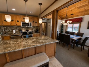 A kitchen with granite countertops, wooden cabinets, a microwave, and a dining area with a table and chairs. - Cozy Condo Across from Main Village & Slopes, Pool/Spa/Workout Included (Durango)