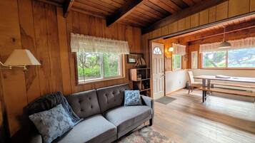 L’intérieur d’un chalet en bois, avec un canapé, une table à manger et une vue sur la verdure environnante.