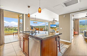 Une cuisine moderne dotée d’un grand îlot central, d’un coin repas offrant une vue agréable et d’un vaste espace de vie agrémenté d’un ventilateur de plafond.
