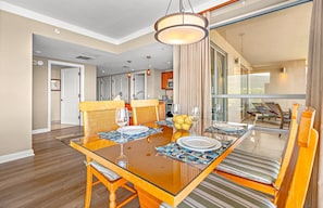 Une salle à manger avec une table en verre, des chaises en osier et une vue sur un balcon agrémenté de fauteuils de relaxation.