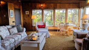 Un intérieur de chalet chaleureux, avec un revêtement mural en bois, un canapé, un fauteuil, une table à manger et une table basse.