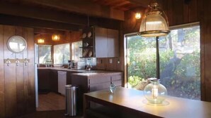 Une cuisine moderne avec des meubles en bois, un évier en acier inoxydable et une grande fenêtre donnant sur un paysage verdoyant.