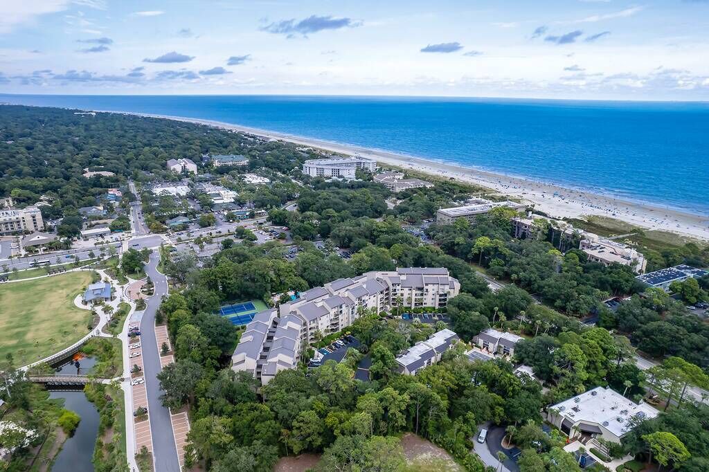 An aerial view of a coastal residential area with a beach, green spaces, and multi-story buildings.
