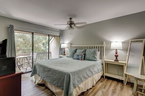 A bedroom with a bed, a ceiling fan, a bedside table with a lamp, a dresser, and a large window.