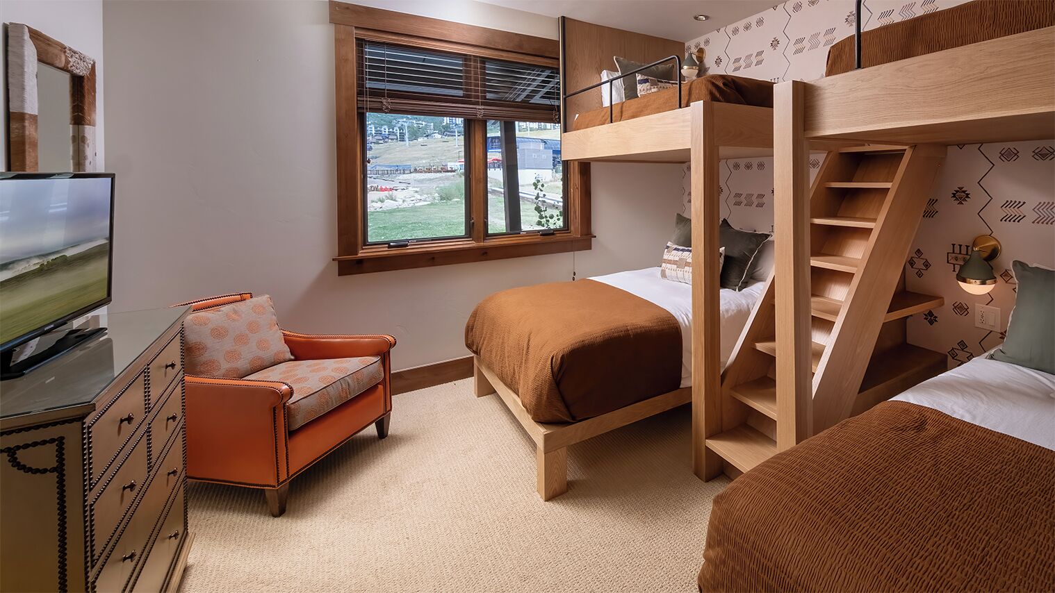 A bedroom with bunk beds, a TV, a chair, and a window with blinds.