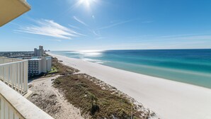 A beach view with a clear sky, a sandy beach, and a building with multiple floors.