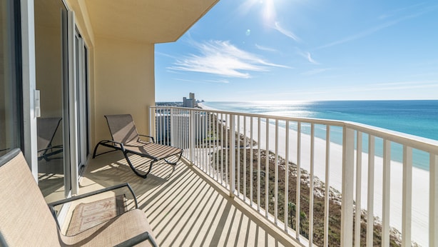 A balcony with a view of the beach and ocean, featuring two chairs and a table.