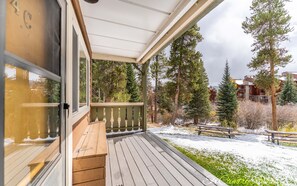 A wooden deck with a railing, a bench, and a view of a snowy landscape with trees and buildings in the background.
