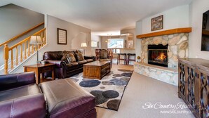 A cozy living room with a fireplace, leather furniture, and a staircase.