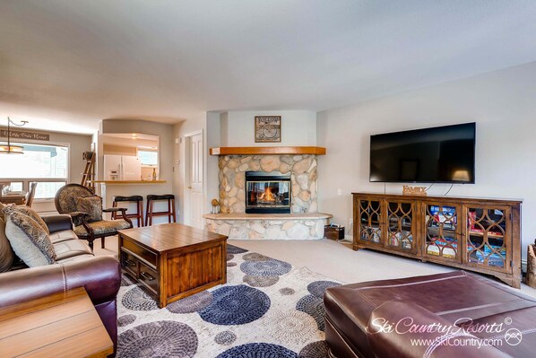 A living room with a stone fireplace, leather furniture, a flat-screen TV, and a wooden cabinet with glass doors.