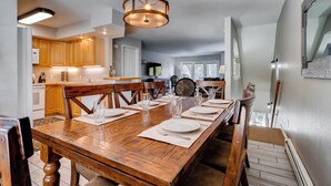 A dining area with a wooden table set for four, a chandelier, and wooden cabinets in the background.