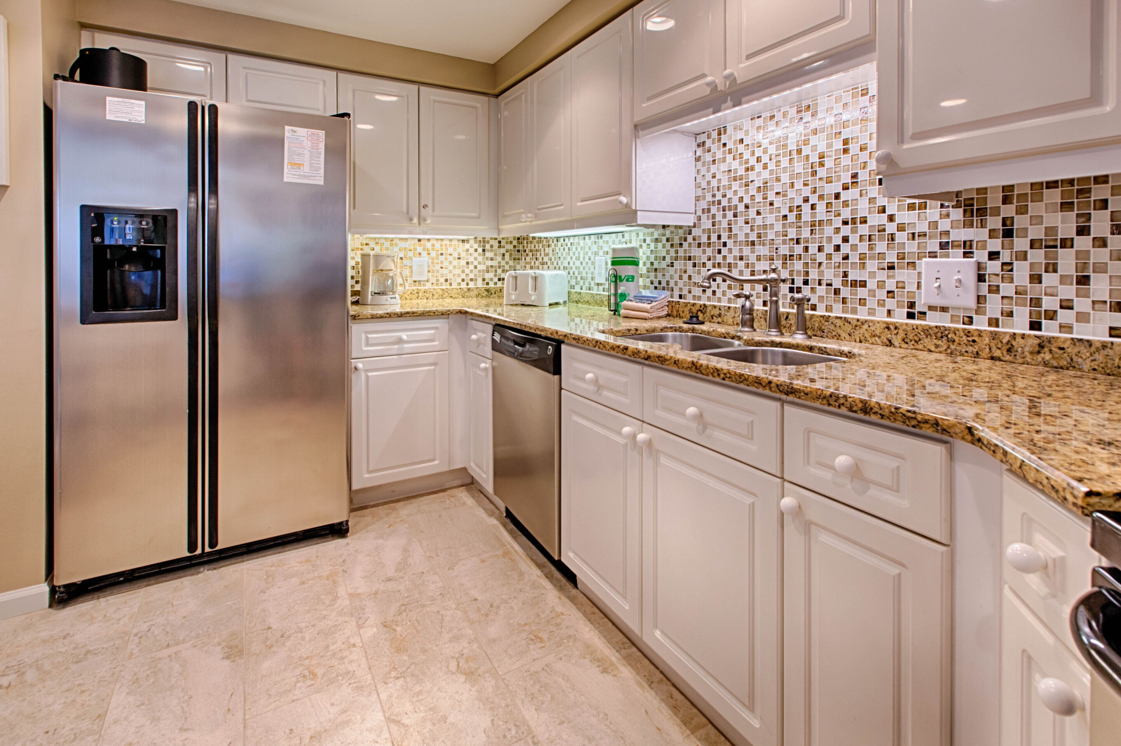 Una cocina moderna con armarios blancos, un refrigerador de acero inoxidable, lavavajillas integrado y encimera de granito.