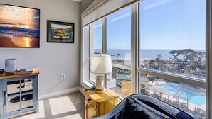 A room with a large window overlooking a pool and ocean view, a desk with a computer, and artwork on the wall. - 4506 Windsor Court - 5th Floor - Serenity at its best.  AMAZING VIEWS! (Hilton Head Island)