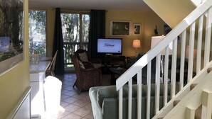 Un salon avec une télévision, un canapé, un fauteuil et un escalier.
