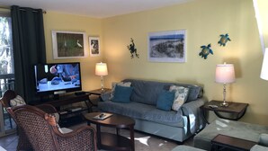 Un salon comprenant un canapé, des fauteuils, une table basse, un téléviseur et des œuvres d’art murales.