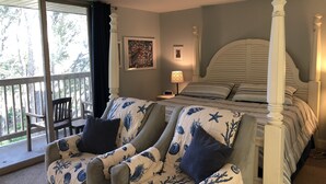 Une chambre à coucher avec un lit à baldaquin, un fauteuil à motifs floraux et une vue sur l’extérieur.