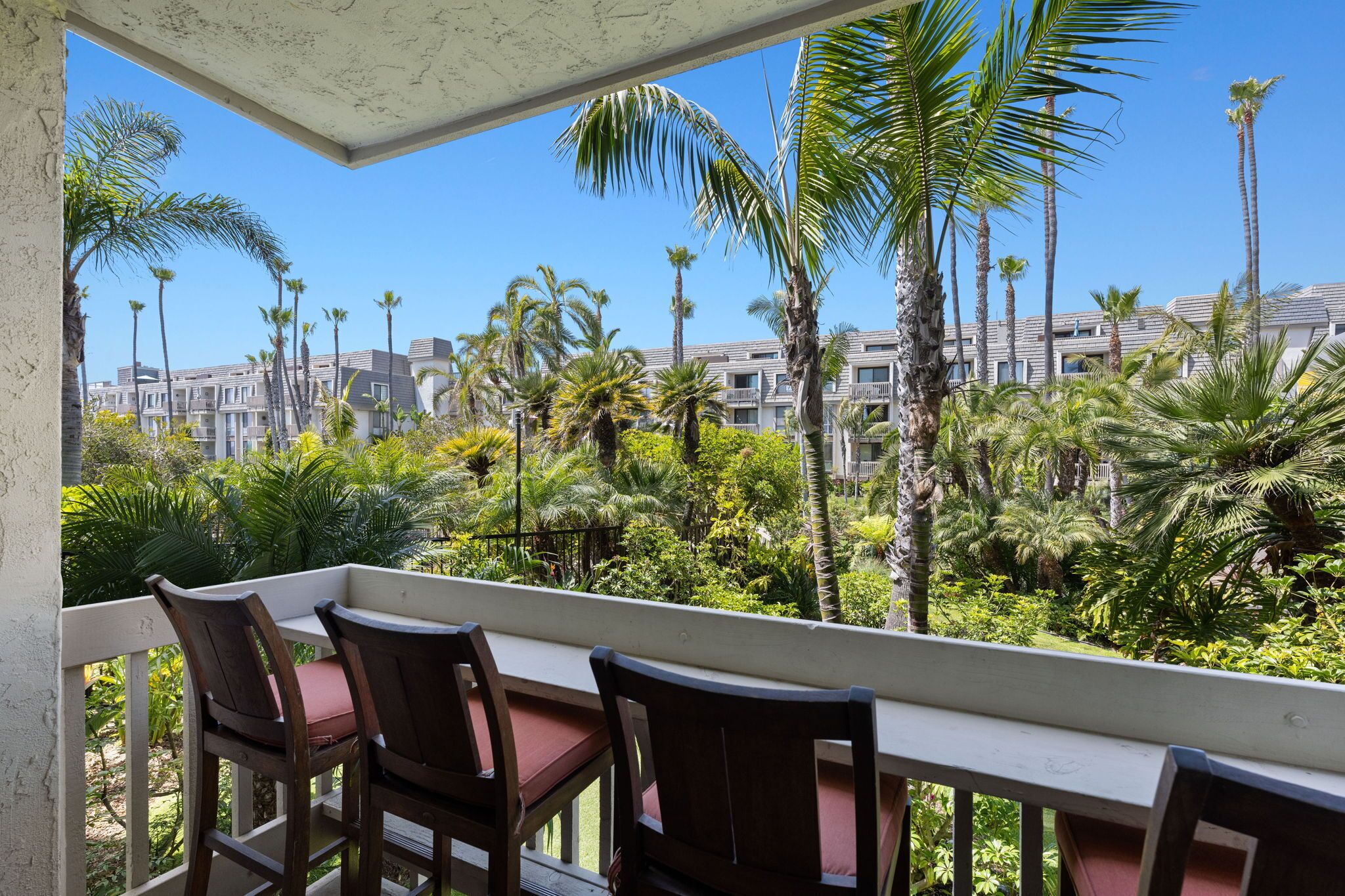 A balcony with a table and chairs, overlooking a residential area with palm trees and buildings.