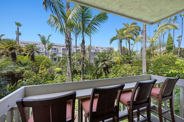 A covered outdoor seating area with a view of a residential building and palm trees.