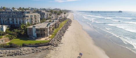 A coastal hotel with multiple buildings, a beach, and a pier in the background.