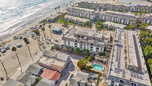Vista aérea de un hotel costero con varias edificaciones, una playa y un puerto deportivo.
