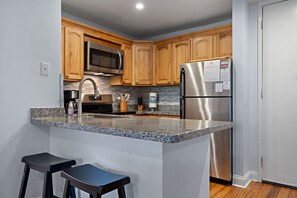 Una cocina moderna con encimeras de granito, electrodomésticos de acero inoxidable, armarios de madera y un microondas integrado.