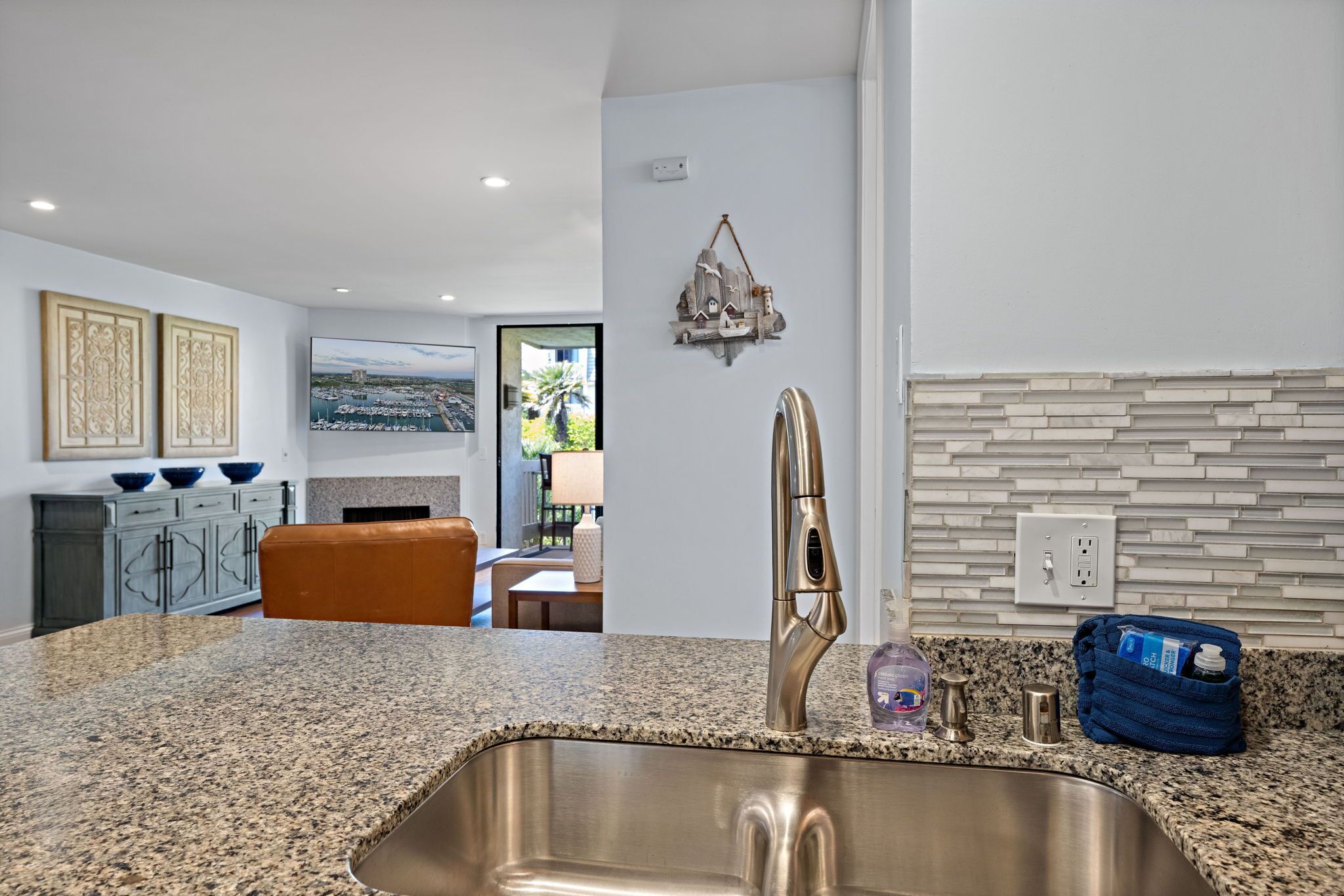 A modern kitchen with a granite countertop, stainless steel sink, and a view of the outdoor patio.